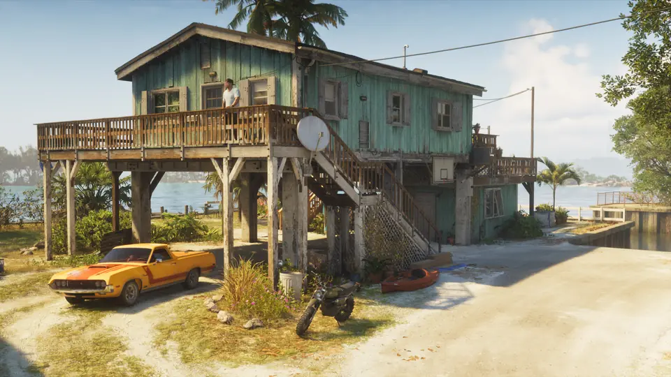 A stilt house by the water with a car and a motorbike outside.